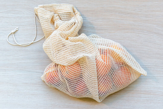 Close-up of a reusable cotton mesh produce bag filled with fruit. Reusable eco-friendly string bag for grocery shopping.