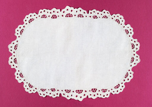 Oval white handmade table napkin with cutwork embroidered lace edge on a pink background. Blank space for text. Close-up, top view, copy space, flat lay, mock up