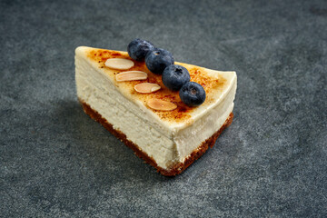Naklejka premium Slice of classic San Sebastian Basque burnt cheesecake decorated with fresh blueberries and almond flakes on dark stone background, gourmet sweet dessert presentation, bakery confectionery photo