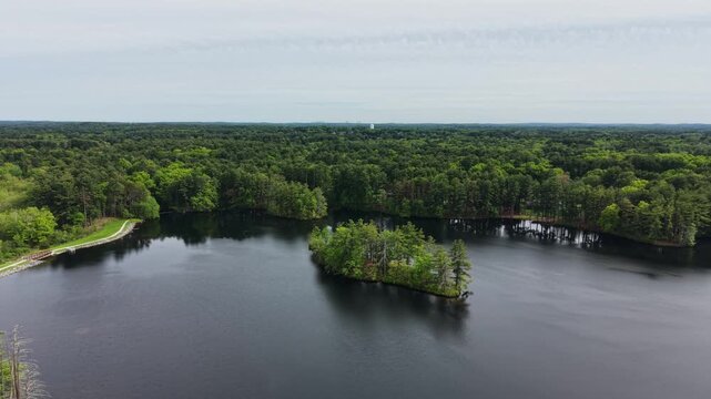 Small islands in lake surrounded by dense green pine forest in Harold Parker State Forest, Andover, Massachusetts, USA. Aerial backward, copy space