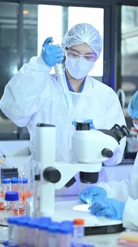Two Female Scientists Working in Modern Research Laboratory with Microscope and Test Tubes