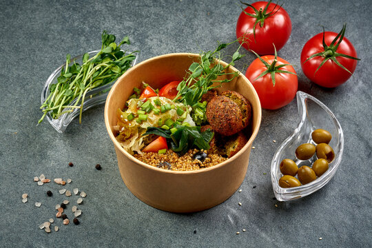 Healthy vegan falafel bowl with quinoa, seaweed wakame, fresh vegetables and green onions in craft paper container, high angle view of Middle Eastern vegetarian food on dark background, takeaway