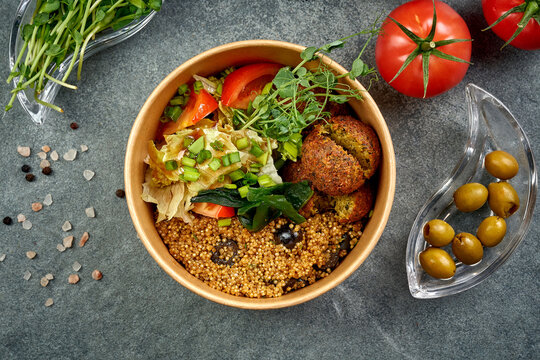 Healthy vegan falafel bowl with quinoa, seaweed wakame, fresh vegetables and green onions in craft paper container, high angle view of Middle Eastern vegetarian food on dark background, takeaway