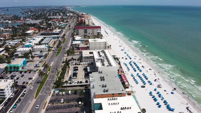 Aerial view capturing a vibrant stretch of beachfront lined with blue parasols and adjacent urban buildings. Ideal for showcasing coastal development or tourism promotions.