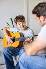 Fototapeta premium Father teaching son playing acoustic guitar at home