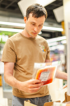 Man comparing packaged food products and reading nutrition label while shopping in supermarket refrigerated section