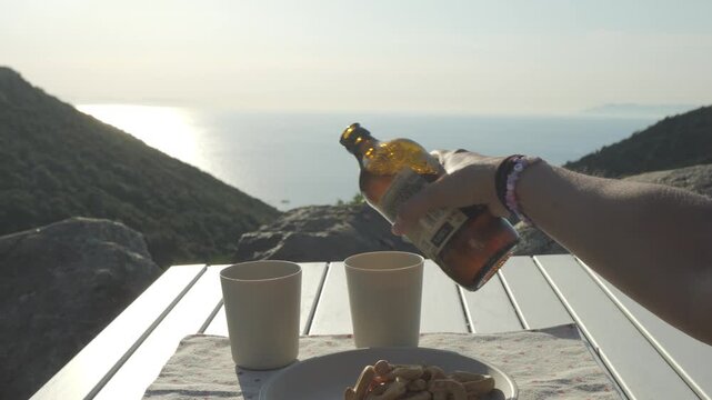 Person holding beer bottle at sunset by the sea, Elba island, Italy