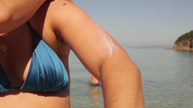Hands applying sunscreen cream on skin at beach, Italy