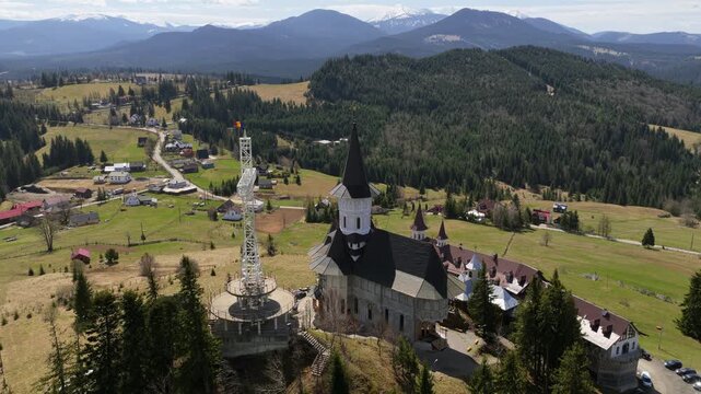 Aerial drone view of the large metal cross and Romanian flag near Acoperamantul Maicii Domnului Monastery in Dorna Arini