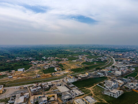 Aerial view of residential houses and green agricultural fields under a cloudy sky near the outskirts of the city Islamabad, Islamabad Capital Territory, Pakistan.