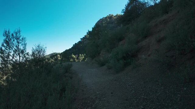 Woman hiking on a mountain trail through scrubby hills under a clear blue sky