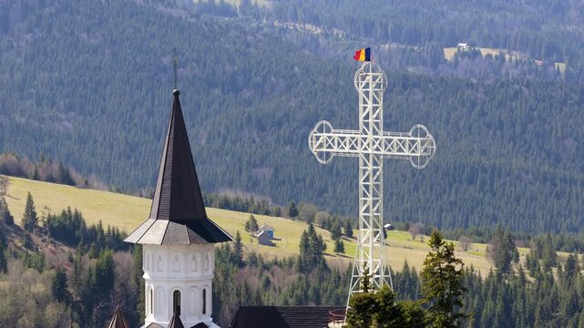 Aerial drone view of the large metal cross and Romanian flag near Acoperamantul Maicii Domnului Monastery in Dorna Arini