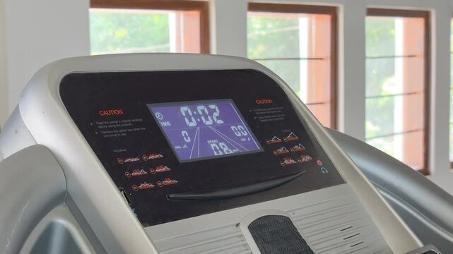 Close up of a modern treadmill control panel in a brightly lit gym interior with digital display showing workout time, speed, and calories for fitness and cardiovascular health training concept