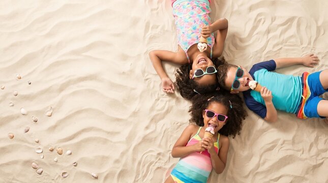 Three children lie on the sand at the beach, eating ice cream. They wear sunglasses and bright clothing. They laugh and enjoy their time outside in the sun