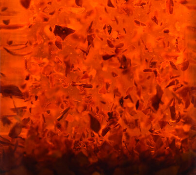 Fiery hot chilli pepper flakes suspended floating in red olive oil.  Cooking ingredient. Elegant, warm, abstract random pattern and texture background. Close up.