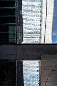 Reflection in a glass facade bends across tower windows, where black and blue contrast turns urban architecture into a layered mirror