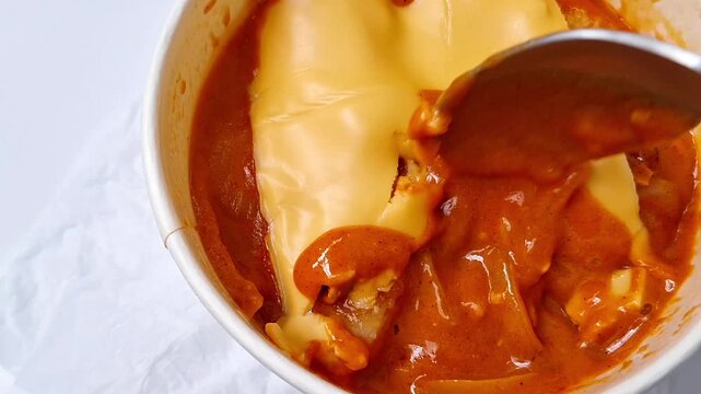 A creamy Korean rose tteokbokki with a melted cheese topping is being stirred slowly.