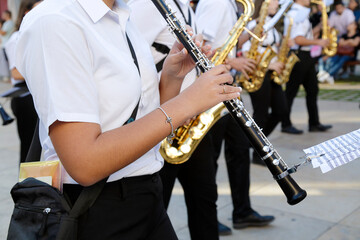 Fototapeta premium A clarinet player in a white shirt and black pants performing outdoors with a marching band, while other musicians with saxophones play in the background
