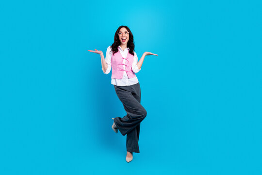 Joyful businesswoman in pink vest posing confidently on blue background, celebrating success and playful professionalism