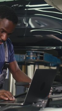 Car mechanic using a laptop to run diagnostic software for troubleshooting engine problems, modern computerised automotive repair.