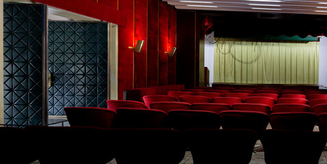 Naklejka premium An empty theater with red velvet seats and a closed curtain awaits its next performance.