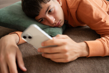 Teenager lying on sofa staring at smartphone screen with absent expression. Concept of screen time, digital habits, social media overuse, boredom and technology dependence. © Elena