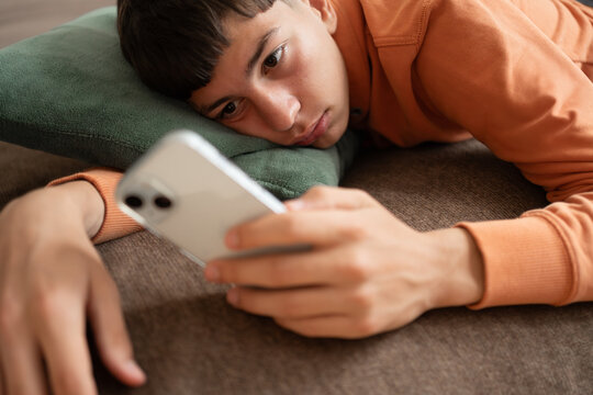 Teenager lying on sofa staring at smartphone screen with absent expression. Concept of screen time, digital habits, social media overuse, boredom and technology dependence.