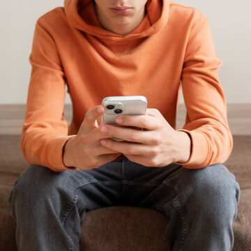 Teenager sitting on sofa and looking at smartphone screen. Modern digital lifestyle, mobile communication, social media use, online activity and everyday technology habits.