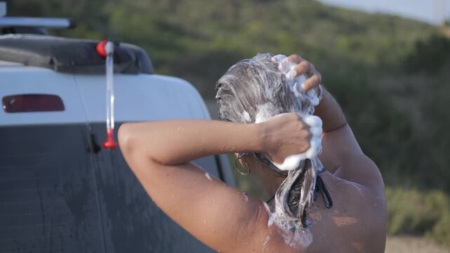 Young woman washing hair outdoors near van, Italy