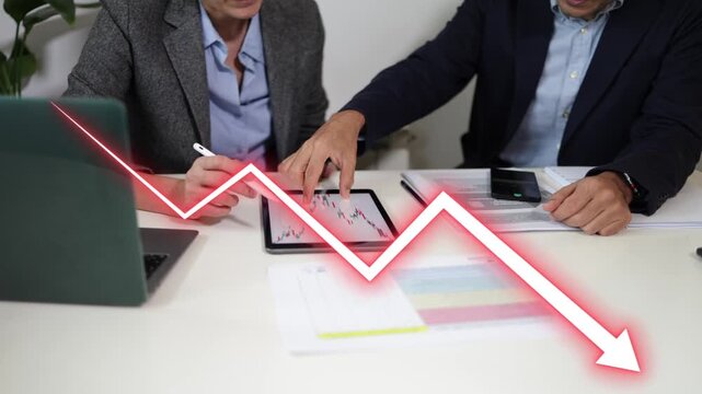 Business colleagues analyzing a descending stock market chart showing financial crisis, recession, inflation, and economic collapse with a red falling arrow on a tablet