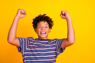Happy excited boy celebrating with raised arms wearing a striped shirt on a bright yellow background expressing joy, victory, confidence and youthful energy © deagreez