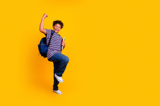 Happy school student jumping with backpack and books on bright yellow background celebrating first day and academic success