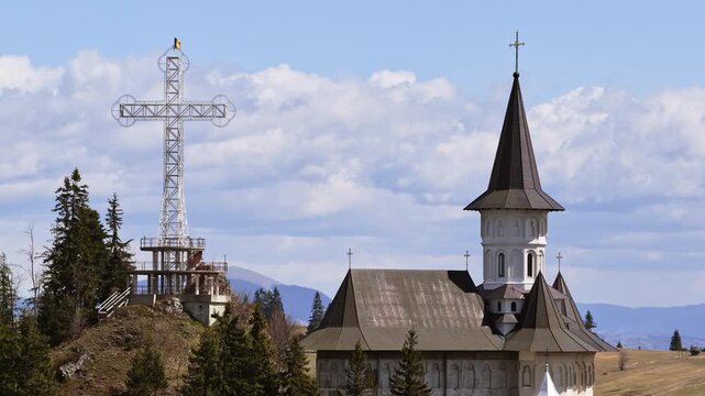 Aerial drone view of the large metal cross and Romanian flag near Acoperamantul Maicii Domnului Monastery in Dorna Arini