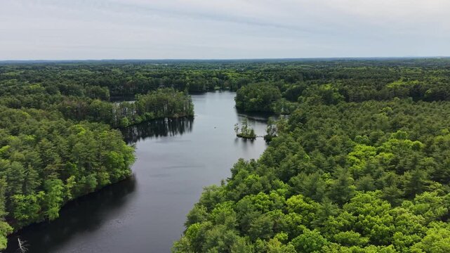 Lake and small islands surrounded by dense green woodland under cloudy sky in Harold Parker State Forest, Massachusetts. Aerial drone panoramic view, copy space
