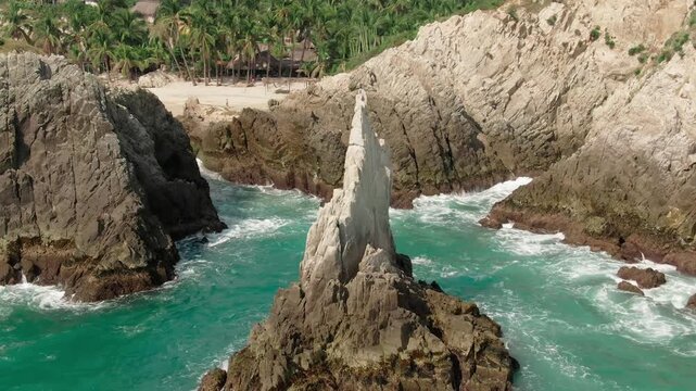 Backward aerial view of Dedo de Dios surrounded by turquoise waves and rugged coastal cliffs in Mexico.