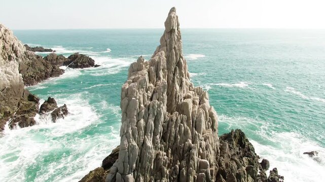 Dedo de Dios sea stack with striking white volcanic rock textures surrounded by turquoise Pacific Ocean waters, and rugged coastal scenery near Maruata Beach, Michoac&aacute;n, Mexico.