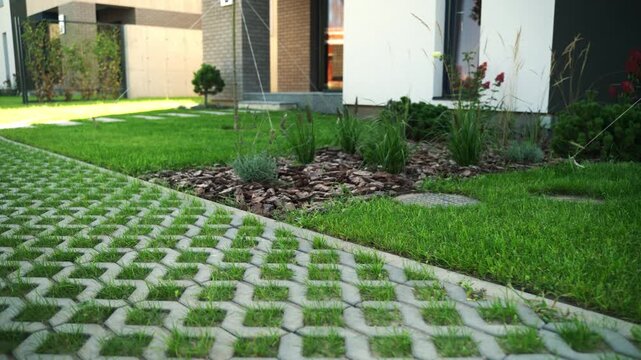 Slow camera movement revealing the backyard of a modern residential house with a lawn, flowerbed, and a driveway made of permeable pavers with grass growing through them