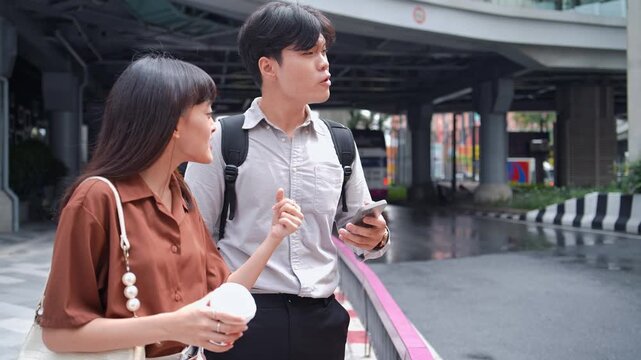 Asian businessman and businesswoman use mobile phone outdoor. Young corporate professional worker look at smartphone screen, gesture, talk, and check travel location map together on urban city street