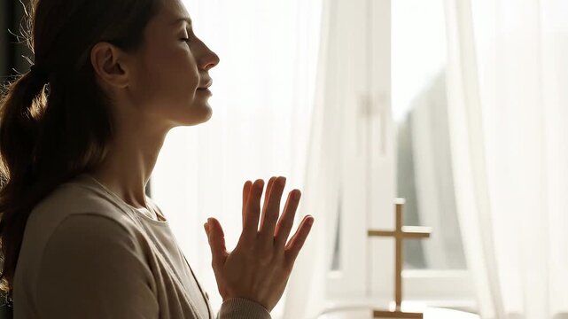 Peaceful woman praying beside a cross in bright church window light