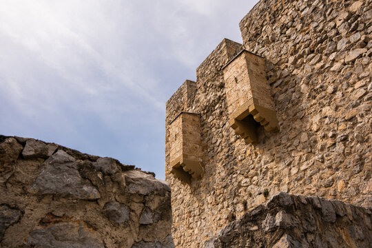 Low angle view of medieval stone fortress wall with ancient machicolations under a cloudy sky