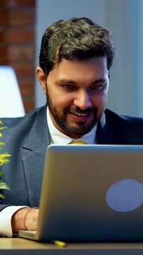Businessman celebrating success with laptop computer at office desk, Indian Asian corporate executive raises fist with joy and achievement, symbol of business victory, motivation, professional growth