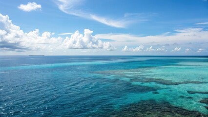 Clear blue ocean water with coral reefs beneath a partly cloudy sky on a sunny day.