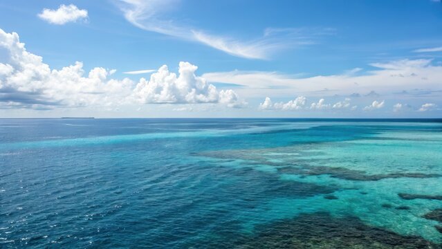 Clear blue ocean water with coral reefs beneath a partly cloudy sky on a sunny day.