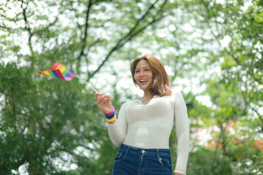 Portrait depicts beautiful beauty surgically enhanced Asian transgender woman holding an LGBTQ pride flag beautiful face lovely smile and a cheerful sensitive demeanor set against backdrop lush garden