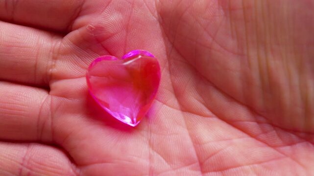 Cinematic macro shot of a pink glass heart in a hand.Soft daylight. Simbol of fragility, emotional support, self-love, empathy, care and vulnerability.