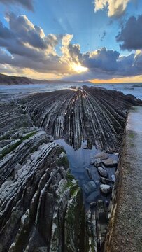 Dramatic crepuscular rays over flysch rock formations at low tide, Zumaia beach, Basque Country, Spain at sunset. Zumaia, Gipuzkoa, Basque Country, Spain