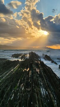 Dramatic crepuscular rays over flysch rock formations at low tide, Zumaia beach, Basque Country, Spain at sunset. Zumaia, Gipuzkoa, Basque Country, Spain
