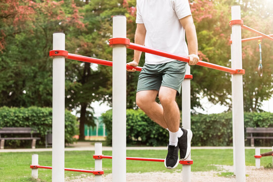 Fit man doing dips on parallel bars at an outdoor sports ground. Bodyweight training, fitness, strength exercise, and active lifestyle