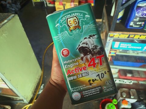 KUALA TERENGGANU MALAYSIA- JUNE 04. 2026.. photo of a hand holding a 1.2 liter can of Justinjarell Active 4T 10W40 fully synthetic motorcycle engine oil in a mechanical repair workshop.