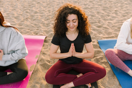 Women friends practising outdoor yoga on beach at sunrise